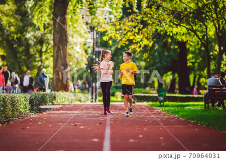 Sports and fitness in adolescence. Caucasian twins boy and girl run on the jogging track in the city park. Two children brother and sister for 10 years running on a rubberized outdoor treadmill Sports and fitness in adolescence. Caucasian twins boy and girl run on the jogging track in the city park. Two children brother and sister for 10 years running on a rubberized outdoor treadmill 70964031