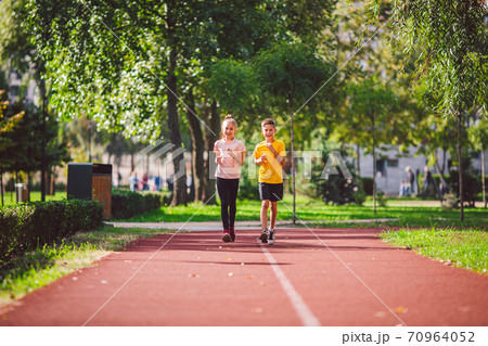 Active recreation and sports children in pre-adolescence. Caucasian twins boy and girl 10 years old jogging on red rubber track through park. Children brother and sister running on treadmill outside Active recreation and sports children in pre-adolescence. Caucasian twins boy and girl 10 years old jogging on red rubber track through park. Children brother and sister running on treadmill outside 70964052