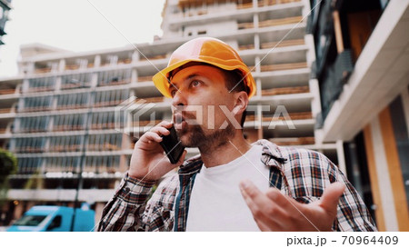 Angry builder, dissatisfied with deadline of work, swears at stress while talking to foreman on phone background of construction site. Wrathful architect, construction engineer talking on cell phone 70964409