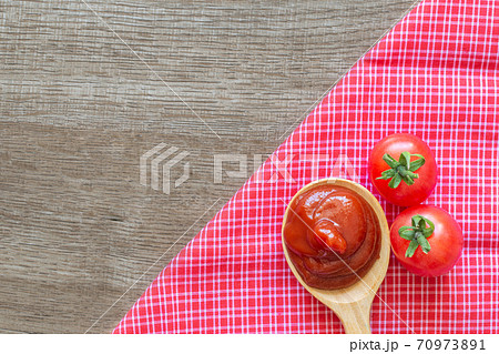 Tomato ketchup sauce in wooden spoon on placemat with tomatoes over wooden background. 70973891