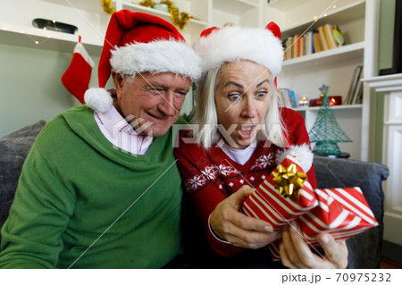 Surprised senior couple opening gift box while sitting on couch at home Surprised senior couple opening gift box while sitting on couch at home 70975232