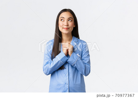 Dreamy beautiful asian woman in blue pajamas looking upper left corner thoughtful, smiling as imaging something before sleep, relish or anticipating, gazing at comment bubble, white background 70977367