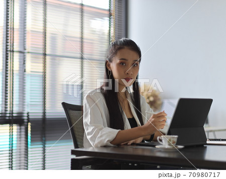Female office worker looking into camera while working with tablet in office room 70980717