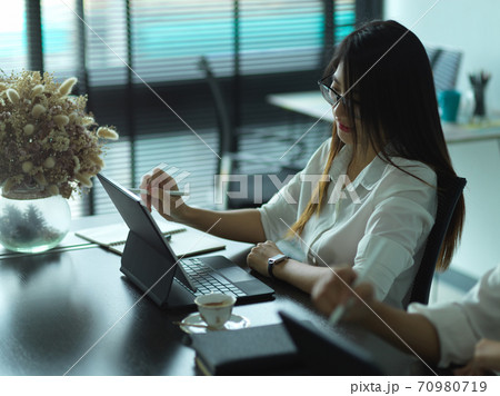 Female office worker concentrating on her tablet while meeting with colleagues Female office worker concentrating on her tablet while meeting with colleagues 70980719
