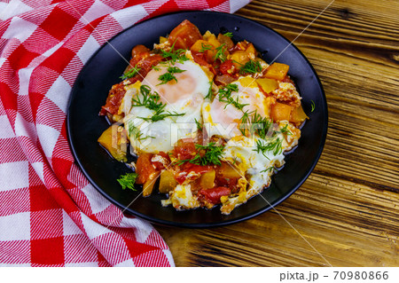 Homemade breakfast shakshuka - fried eggs, onion, bell pepper, tomatoes and dill on rustic wooden table. Jewish cuisine 70980866