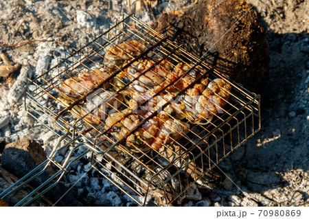 Grilling catfish slices in portable barbecue grill on campfire 70980869