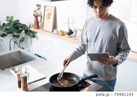 自宅でレシピを見ながらステーキを焼く若い男性 自宅でレシピを見ながらステーキを焼く若い男性 70981193