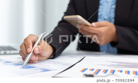 Financial businessmen use mobile phones to calculate income and analyze data about the company's financial performance to prepare for presentation to customers, Tax and accounting system concept. Financial businessmen use mobile phones to calculate income and analyze data about the company's financial performance to prepare for presentation to customers, Tax and accounting system concept. 70982894