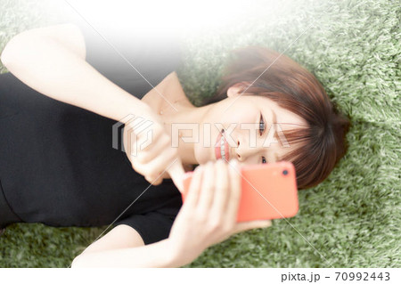 寝転んでスマホを見る若い女性 70992443