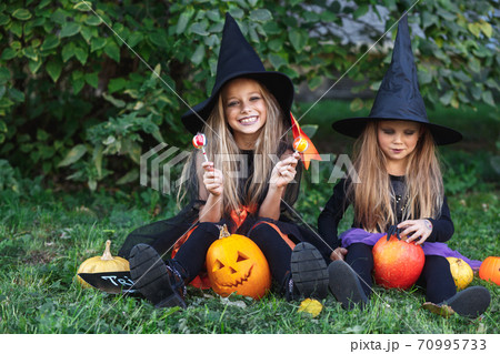 Two funny little girls in witch costumes eating Halloween candy Two funny little girls in witch costumes eating Halloween candy 70995733