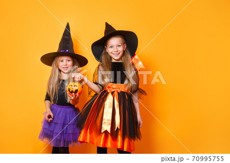 Portrait of two funny little girls dressed up as halloween witch on orange background 70995755