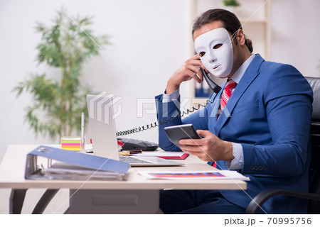 Male employee with mask in hipocrisy concept Male employee with mask in hipocrisy concept 70995756