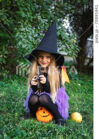 Funny child girl in witch costume for Halloween sitting on pumpkin Jack outdoor Funny child girl in witch costume for Halloween sitting on pumpkin Jack outdoor 70995841