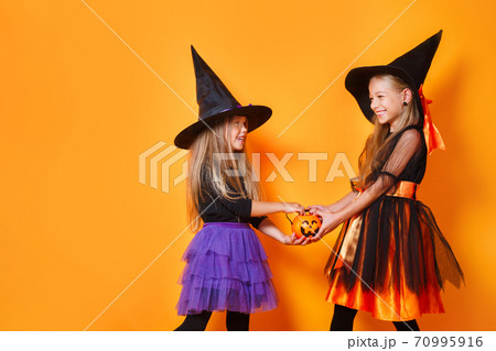 Happy child girls in witch costumes on orange background Happy child girls in witch costumes on orange background 70995916