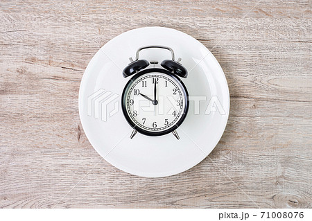Top view alarm clock on white plate on wooden table background. Intermittent fasting, Ketogenic dieting, weight loss, meal plan and healthy food concept Top view alarm clock on white plate on wooden table background. Intermittent fasting, Ketogenic dieting, weight loss, meal plan and healthy food concept 71008076