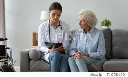 Young female doctor consulting disabled old patient writing in clipboard Young female doctor consulting disabled old patient writing in clipboard 71008140