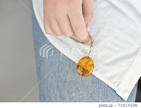 female hand holding a gold chain with amber pendant.  71014106