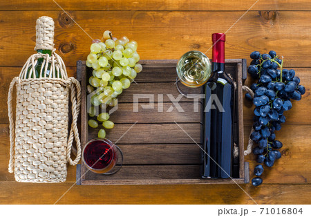 Two bottles with glasses of wine and grapes on a wooden background. Two bottles with glasses of wine and grapes on a wooden background. 71016804