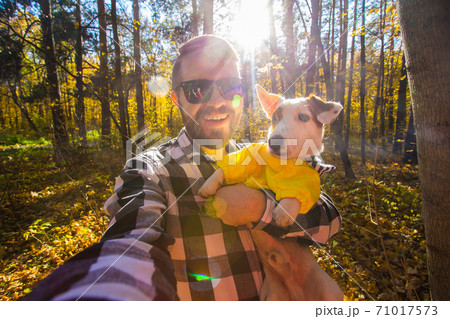 Man taking selfie with his dog at autumn park. Guy posing with jack russell terrier for a picture on the mobile phone outdoors. Pet and people concept. 71017573