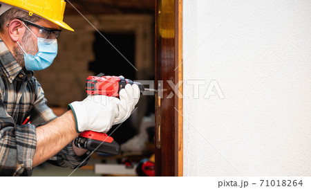 Carpenter at work protects the face with the surgical mask. Covid-19 prevention. Carpenter at work protects the face with the surgical mask. Covid-19 prevention. 71018264