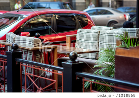 A street cafe table and chairs with soft cushions, an institution fenced with railings from cars that stand against the table. A street cafe table and chairs with soft cushions, an institution fenced with railings from cars that stand against the table. 71018969