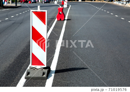 New asphalt pavement and fresh road markings with a white-red safety sign enclosing oncoming traffic. 71019576