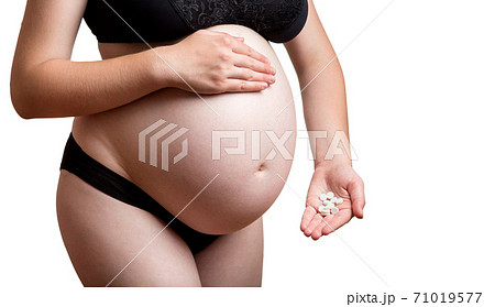 Medical theme with a pregnant woman no face in black underwear holding in her hand a bunch of white round pills close-up on a white background with copy space for text. 71019577