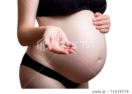 A pregnant woman with a belly holds an ampoule with a medicinal medicine in her hand isolated on white background. 71019578