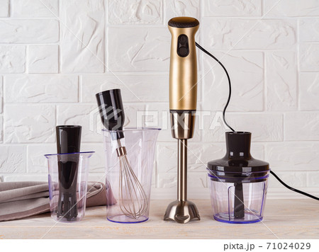 Immersion hand blender with different attachments and two cups on wood table.  71024029