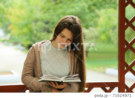 A young girl with long hair reads a book in the Park.  71024971