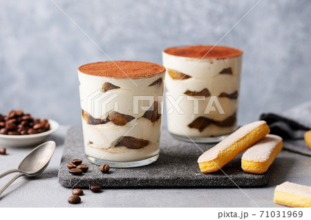 Tiramisu dessert in glass on cutting board. Grey background. Close up. 71031969