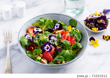 Fresh green salad with strawberries and edible flowers in a bowl. Marble background. Close up. 71032012
