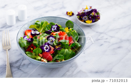 Fresh green salad with strawberries and edible flowers in a bowl. Marble background. Copy space. 71032013