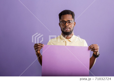 Picture of young african american man holding blank board on violet background 71032724