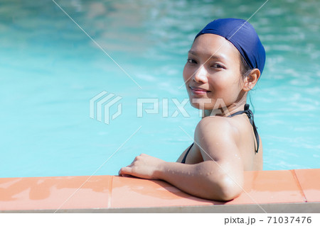 Girl in bikini and swimming cap leaning on the edge of the pool 71037476