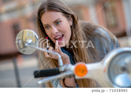 Woman looking at a rear-view mirror while applying a lipstick 71038995