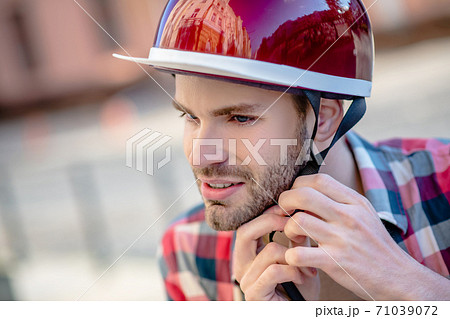 Man putting on a red helmet while riding a scooter 71039072