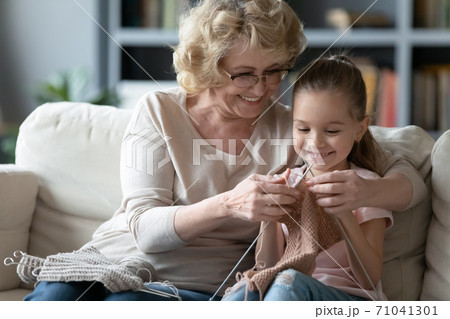 Happy proud elderly retired grandmother teaching little granddaughter creating clothing. Happy proud elderly retired grandmother teaching little granddaughter creating clothing. 71041301