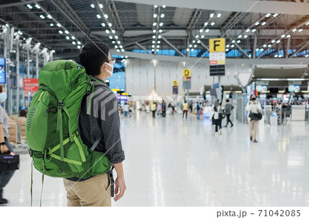 Young man traveler wearing medical face mask and checking flight time in airport terminal, protection Coronavirus disease (Covid-19) infection. New Normal and travel bubble concept 71042085