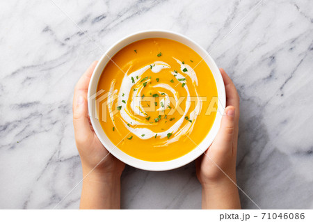 Kids hands holding a bowl with pumpkin soup. Marble background. Top view. 71046086