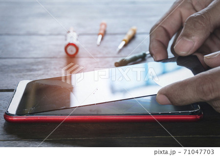 Hand of repairman Phone screen cracking repairs for smartphone By professional technician with mini tools and orange light on the desk. Hand of repairman Phone screen cracking repairs for smartphone By professional technician with mini tools and orange light on the desk. 71047703