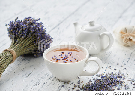 Healthy lavender herbal tea cup, dry lavender flowers and tea kettle on white wooden table. Healthy lavender herbal tea cup, dry lavender flowers and tea kettle on white wooden table. 71052263
