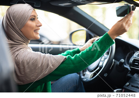 Young muslim woman driving alone adjusting rearview mirror Young muslim woman driving alone adjusting rearview mirror 71052448