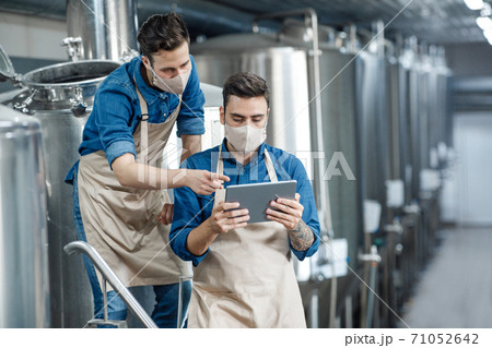 Brewery workers enter data at tablet and operate equipment Brewery workers enter data at tablet and operate equipment 71052642