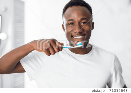 Happy African American Man Cleaning Teeth Standing In Bathroom Happy African American Man Cleaning Teeth Standing In Bathroom 71052643