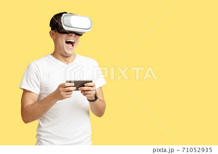 Happy young man with open mouth in virtual reality glasses holds smartphone and play Happy young man with open mouth in virtual reality glasses holds smartphone and play 71052935