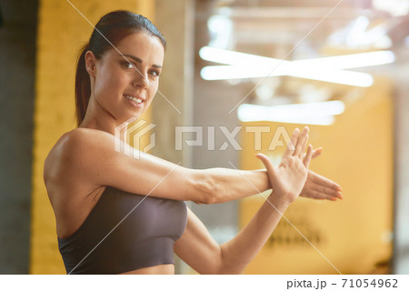 Young beautiful fitness woman in sportswear stretching muscles and looking at camera, warming up before workout at gym 71054962