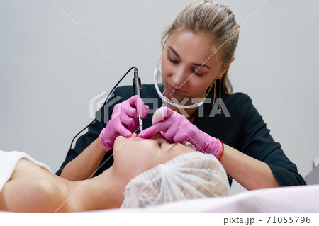 Cosmetology cabinet client lies on couch. Beautician applies marking on eyebrows. Cosmetology cabinet client lies on couch. Beautician applies marking on eyebrows. 71055796