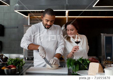 Handsome young African chef is cooking together with his Caucasian girlfriend in the kitchen using red wine as an ingredient. Handsome young African chef is cooking together with his Caucasian girlfriend in the kitchen using red wine as an ingredient. 71055870