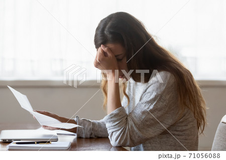 Upset woman sitting at desk holding letter with bad news Upset woman sitting at desk holding letter with bad news 71056088